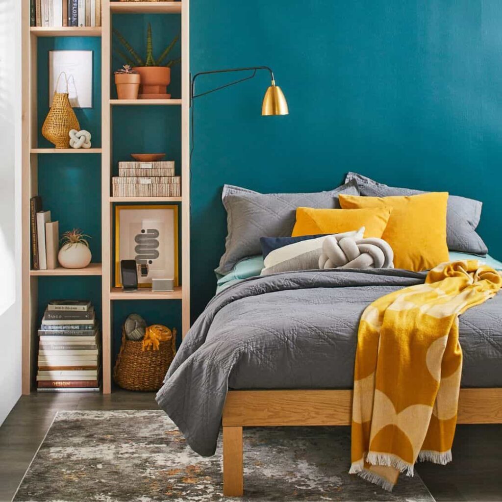 Teal wall with gray bedding and mustard pillows and blankets